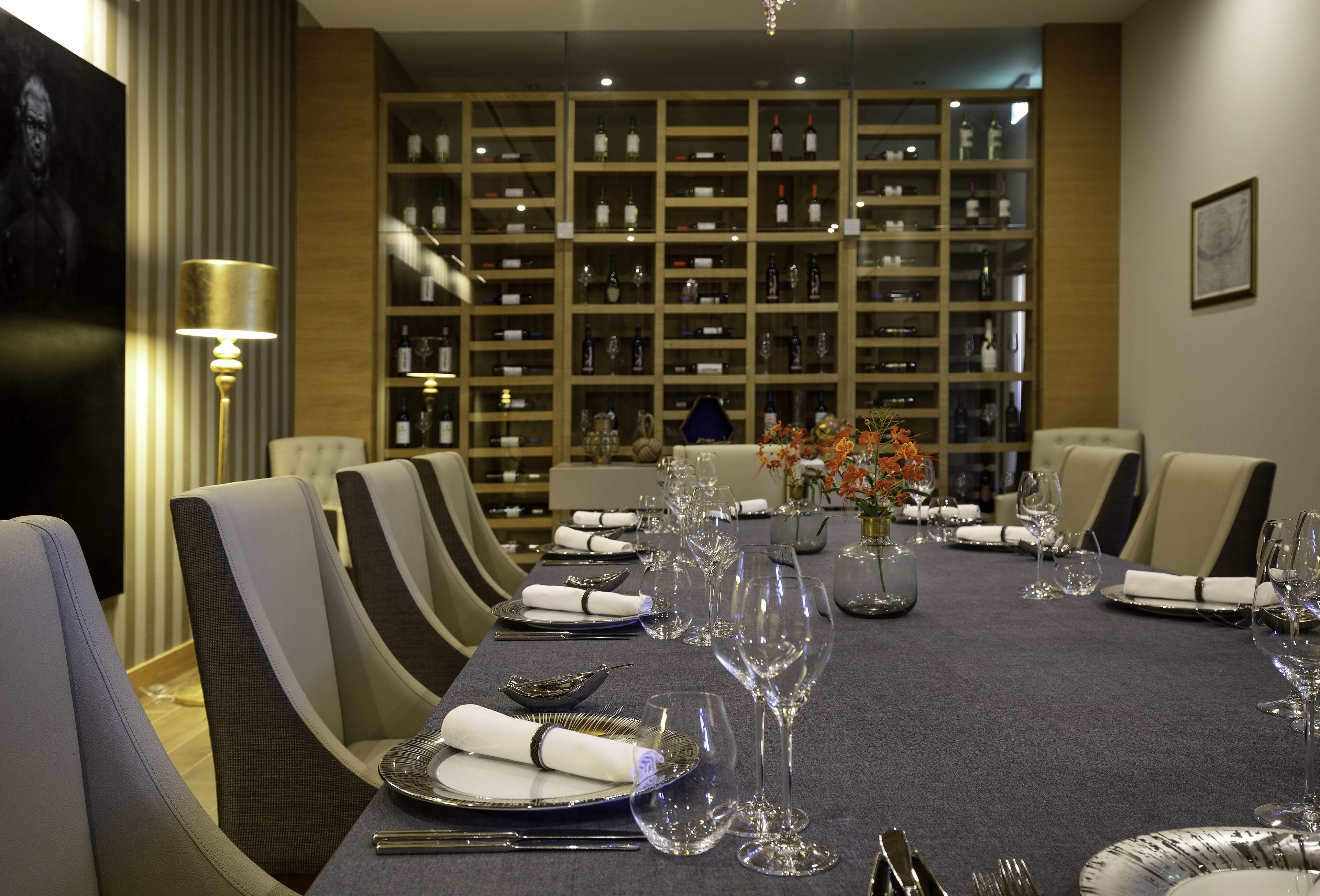 A dining area with a long table set for a meal, surrounded by chairs, and a wine rack in the background.
