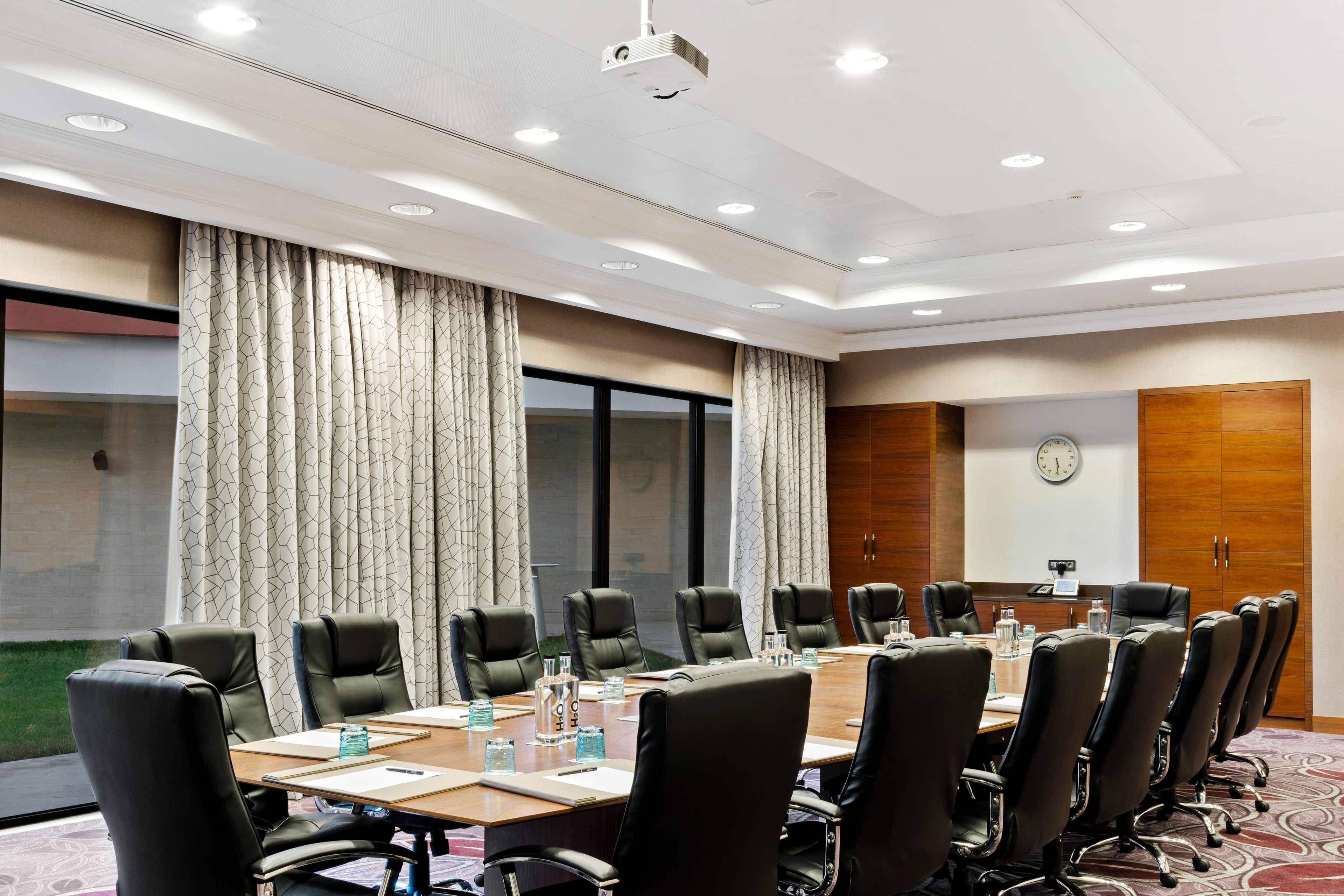 A conference room with a long table, multiple chairs, a clock on the wall, and a projector.