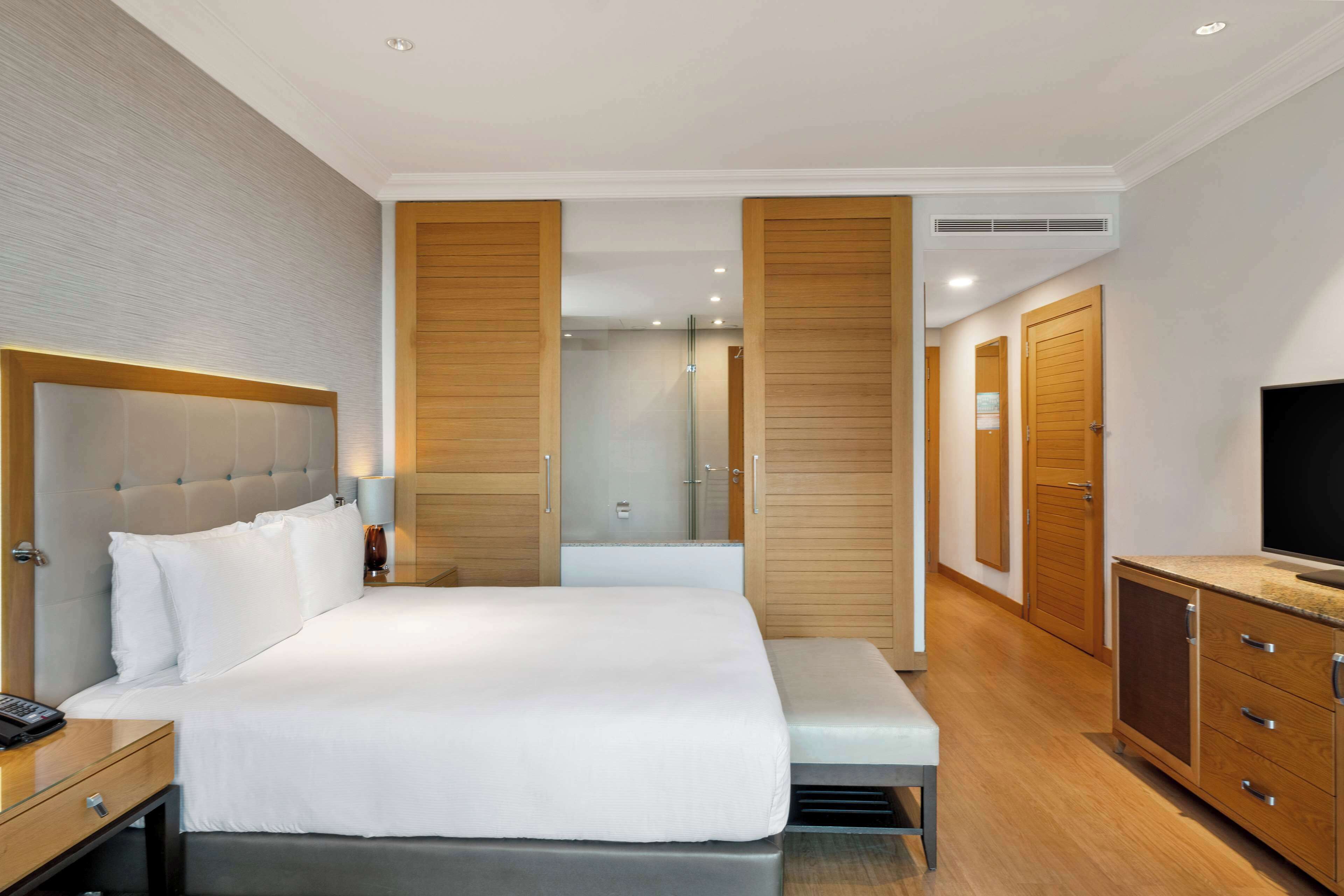 Una habitación de hotel con una cama grande, una mesita de noche con lámpara, un televisor y un armario.