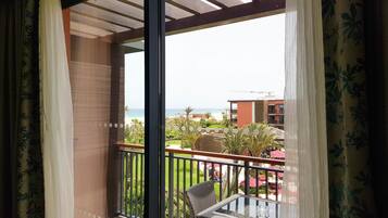 Un balcón con una mesa de vidrio y sillas de mimbre, con vista a una playa y edificios de un complejo turístico.