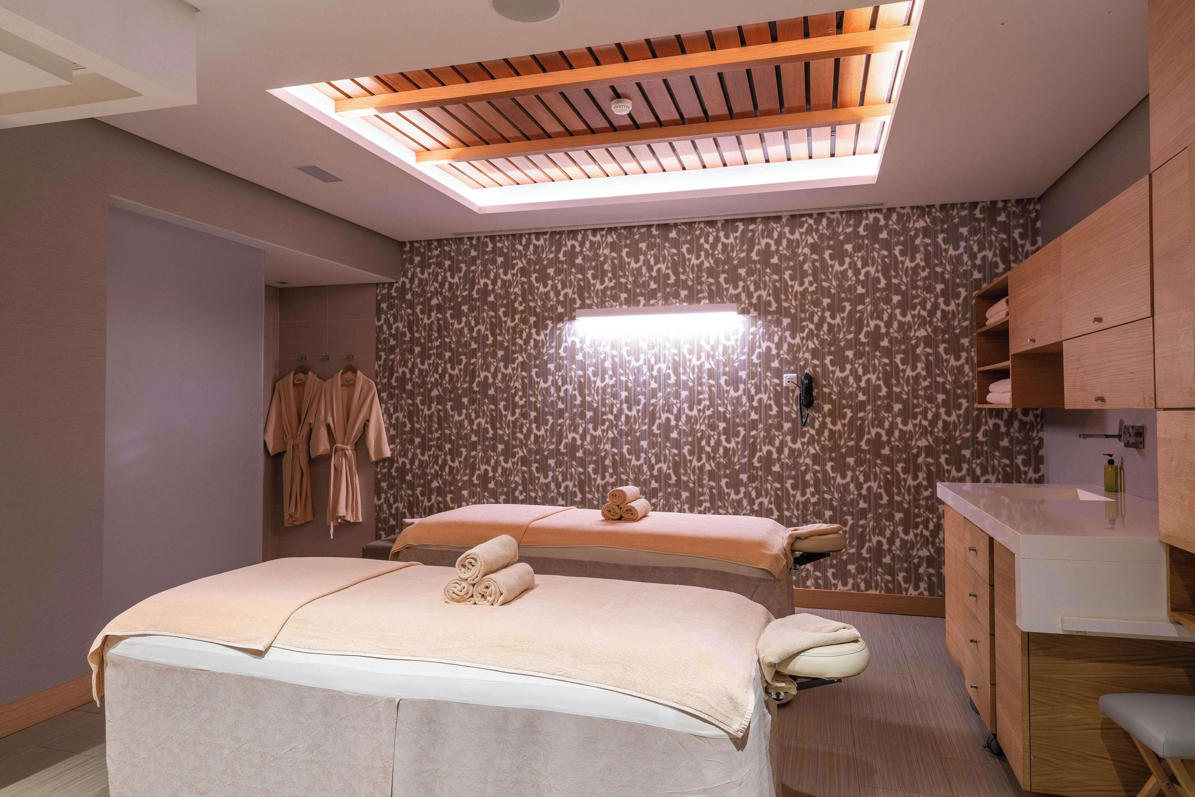 A spa room with two beds, a ceiling skylight, patterned wallpaper, and wooden cabinets.