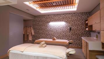 Ein Wellnessraum mit zwei Betten, einem Dachfenster, gemustertem Wandpapier und Holzschränken.