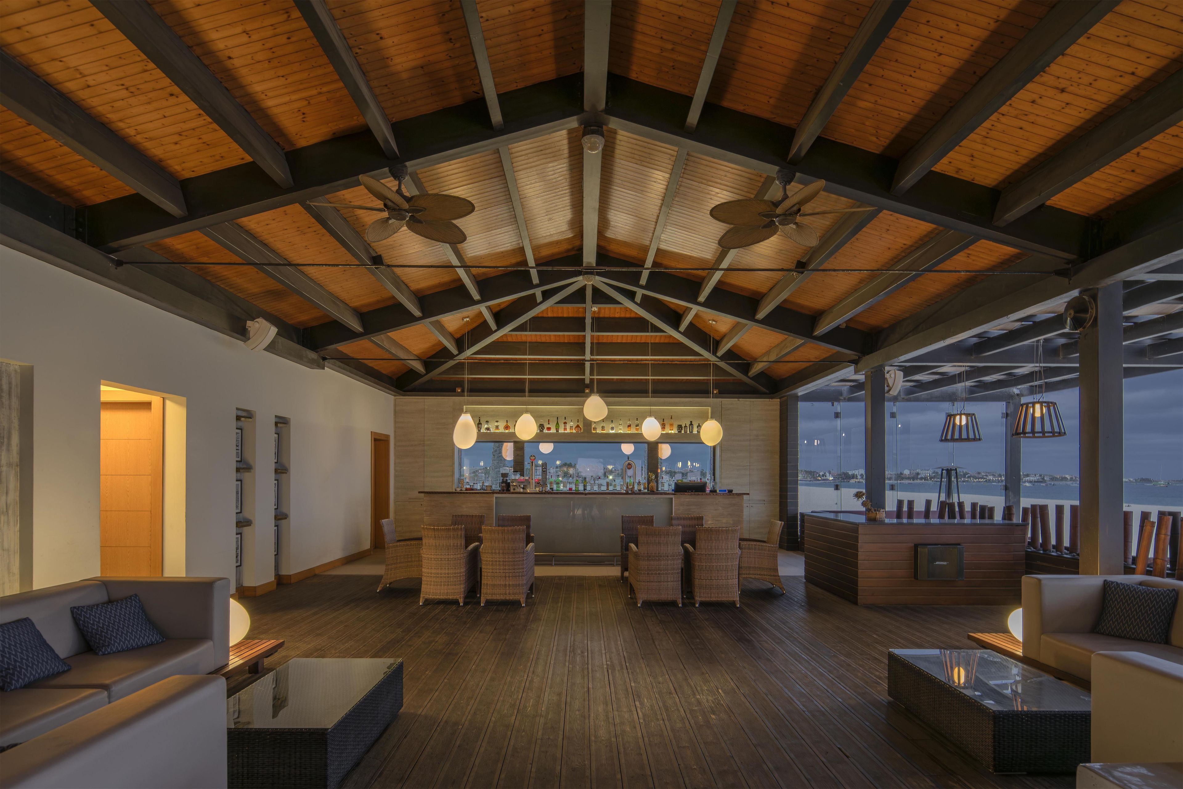 Amplia sala de estar con techo alto, vigas de madera y un bar con vista a la ciudad.