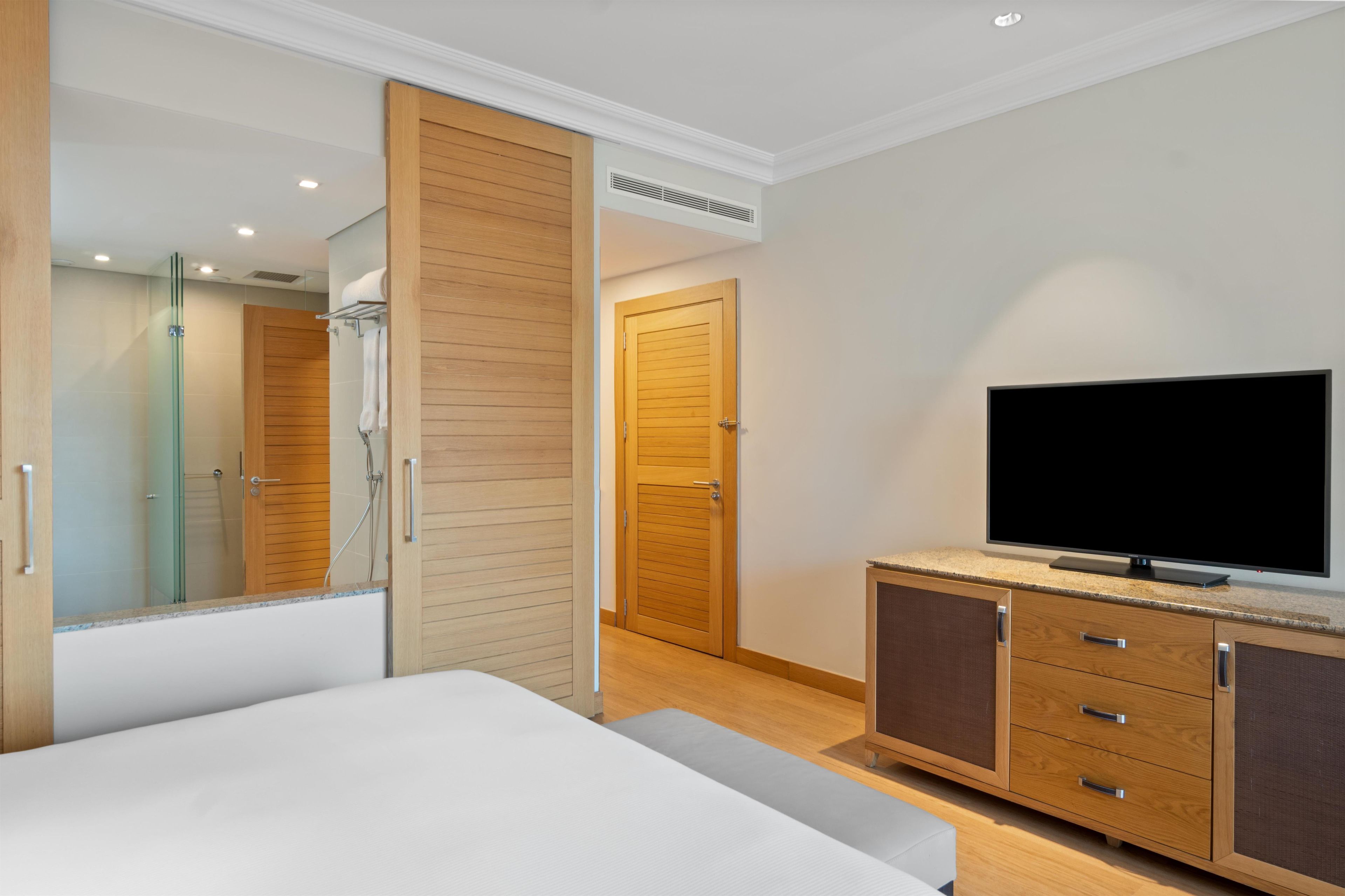 A hotel room with a bed, a television, a wardrobe, and a bathroom with a shower.