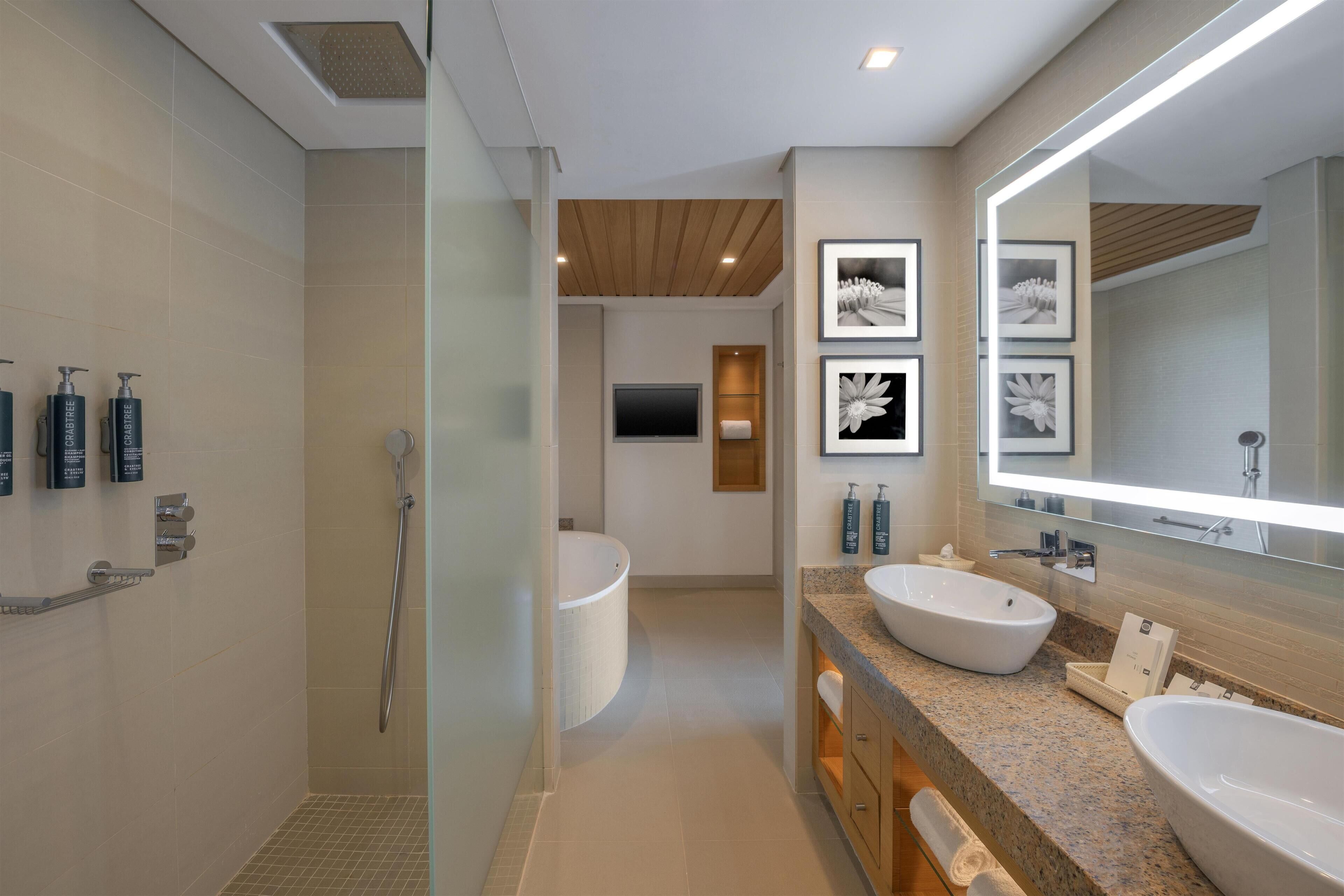 A modern bathroom with a shower, two sinks, a large mirror, and framed artwork on the wall.