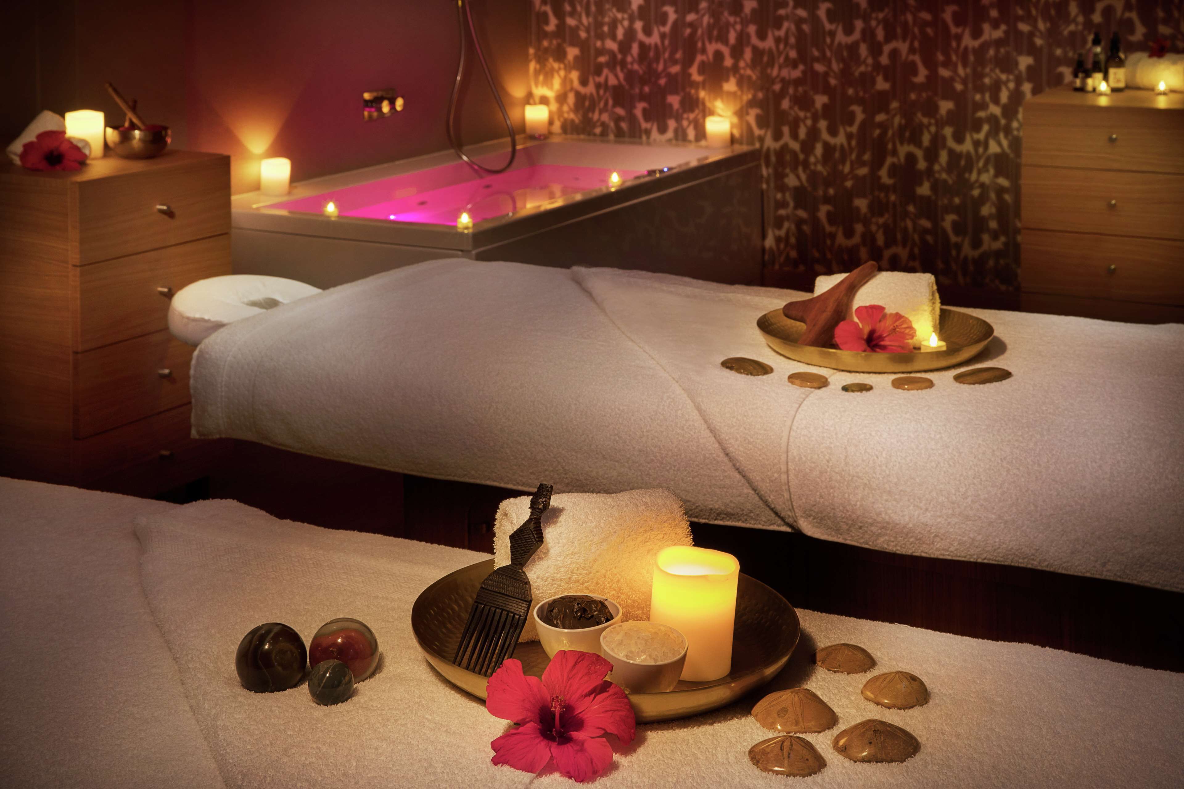 Ein Spa-Raum mit Massagetisch, Kerzen und einer Badewanne.