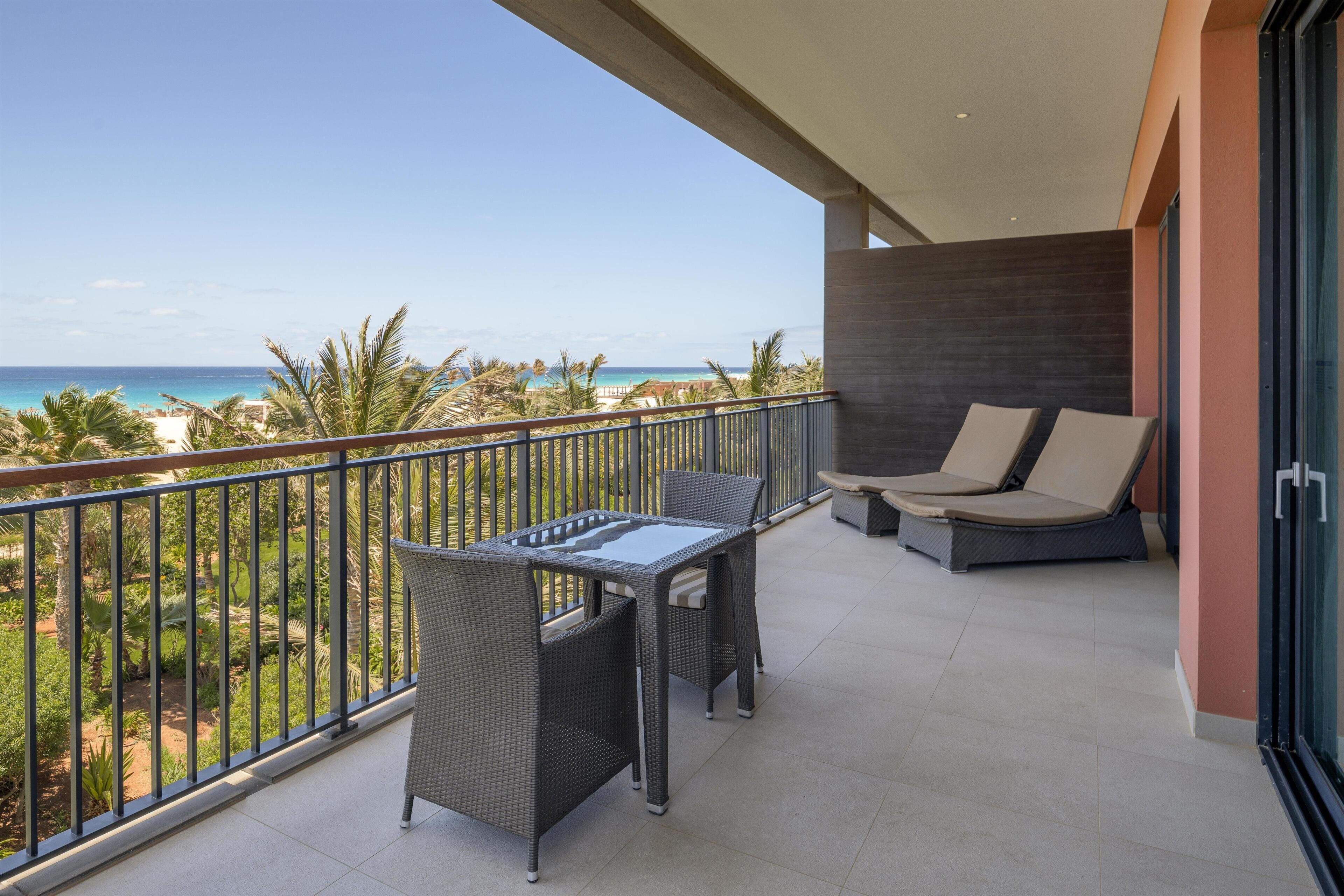Een balkon met een tafel en stoelen, een bank en uitzicht op de oceaan.