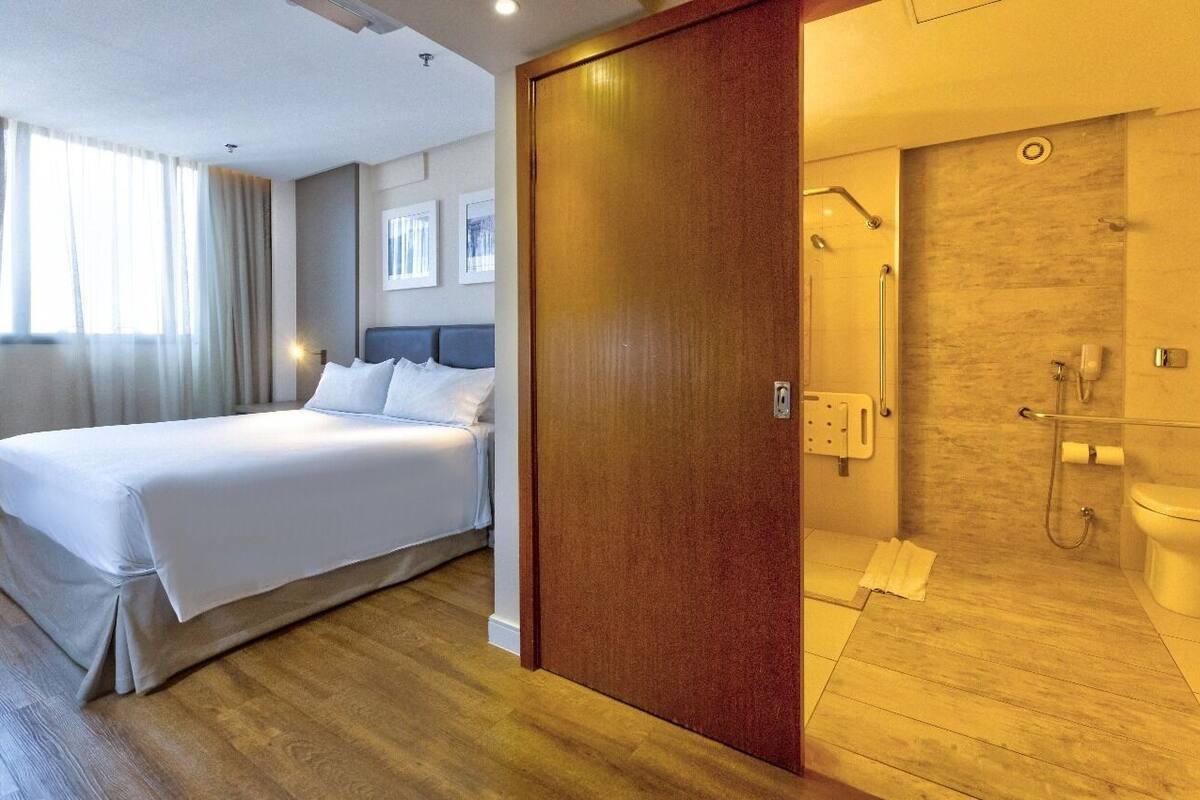 A hotel room with a bed, a wooden floor, a bathroom with a shower, and a toilet.