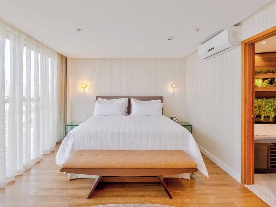 Un dormitorio moderno con una cama grande, un banco, una mesita de noche y aire acondicionado instalado en la pared.