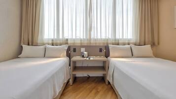 A hotel room with two single beds, a bedside table with a phone and a lamp, and a window with sheer curtains.