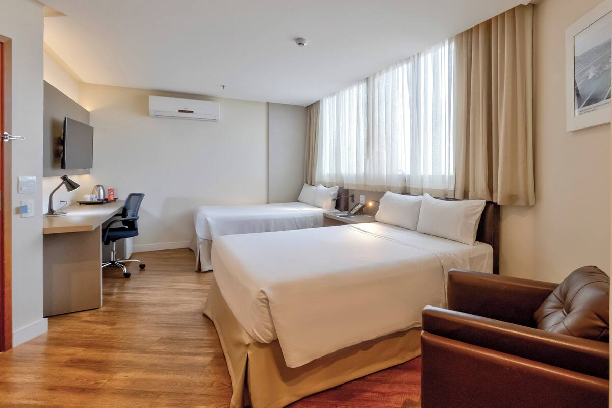A hotel room with two beds, a desk with a chair, a TV, and a window with curtains.