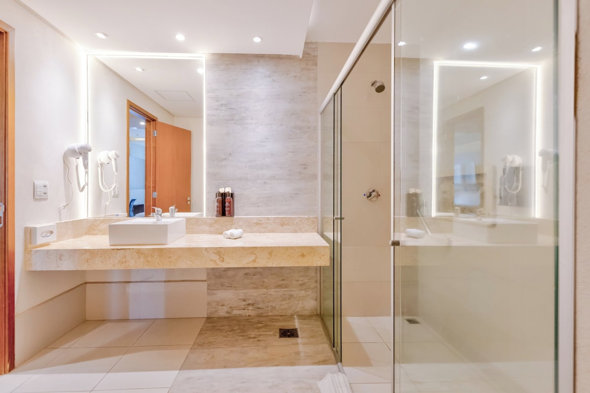A modern bathroom with a large vanity, a glass shower enclosure, and a visible door leading to another room.