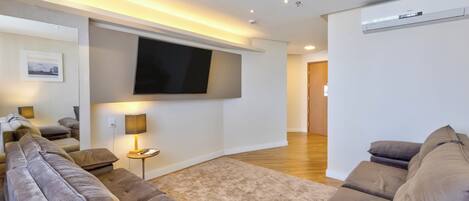 Una sala de estar moderna con un televisor de pantalla plana montado en la pared, un conjunto de sofá, una mesita auxiliar con una lámpara y piso de madera.