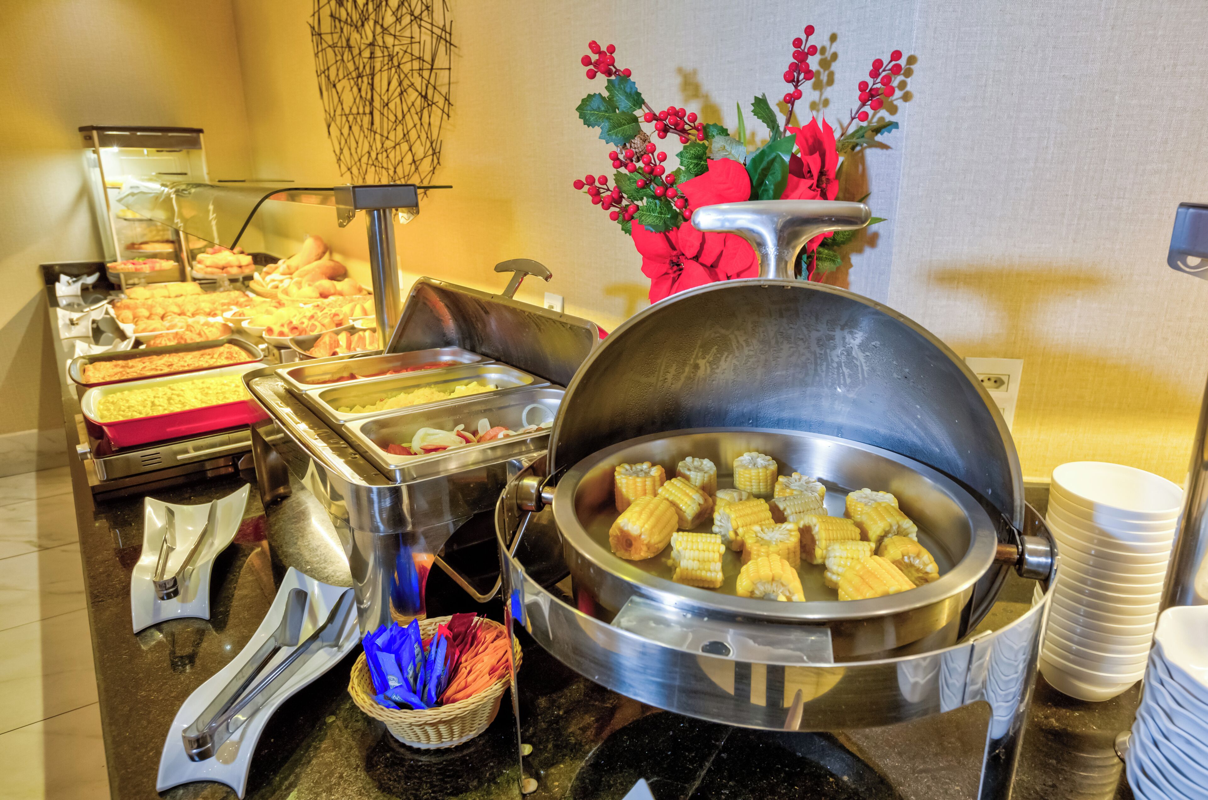 A buffet with various food items, including a large pot of corn on the cob and trays of baked goods.