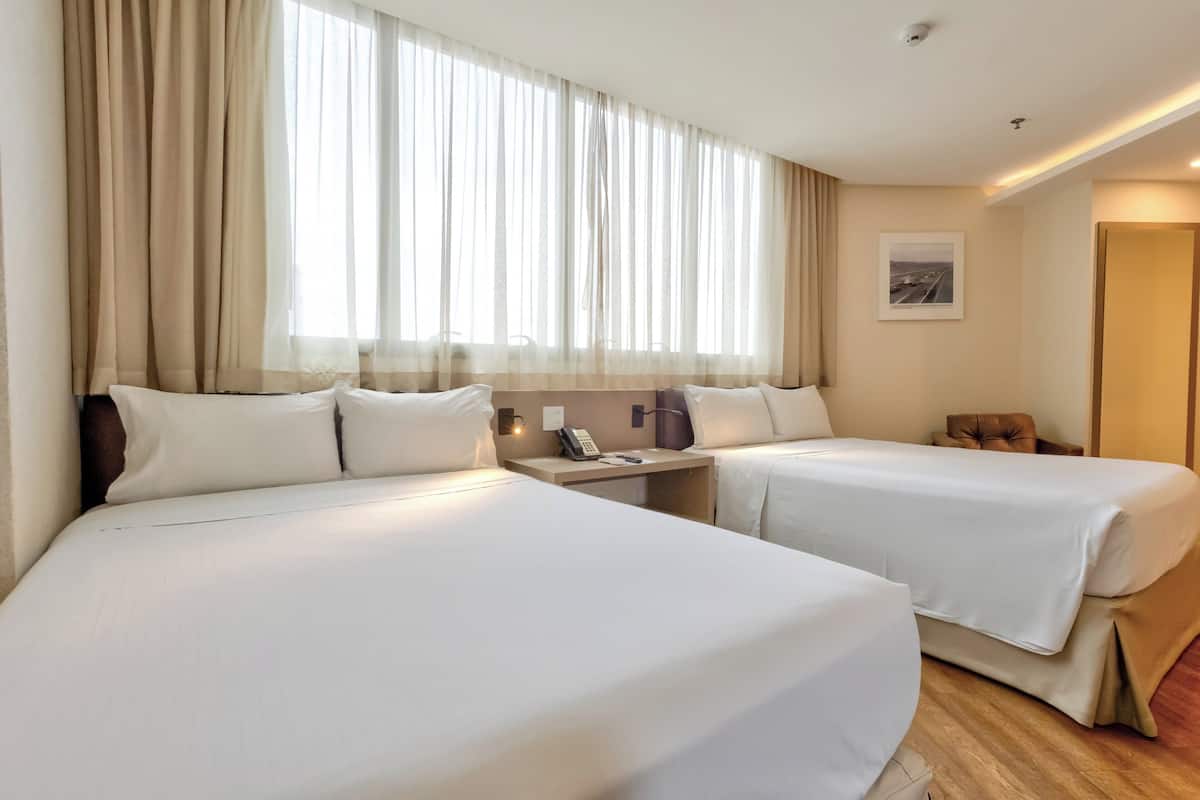 A hotel room with two beds, a nightstand with a phone, and a window with curtains.