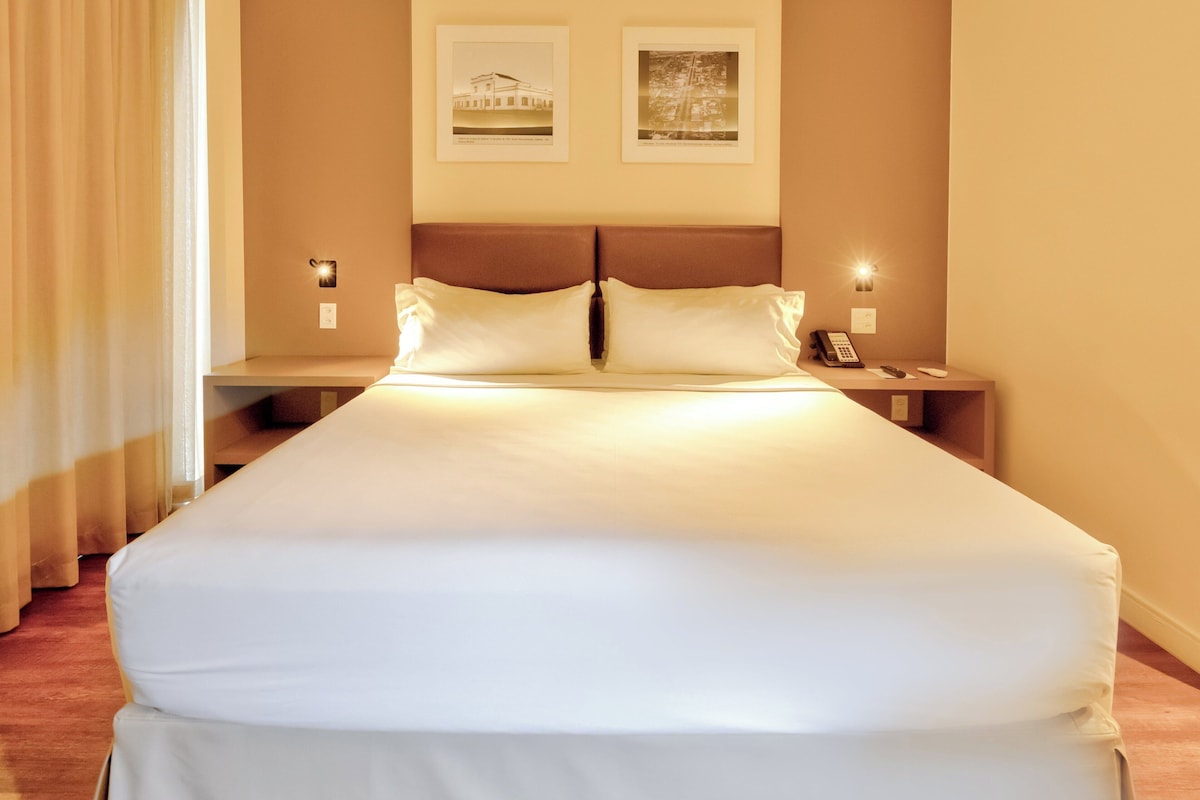 A neatly made bed with white linens, two bedside tables with lamps, and two framed pictures on the wall.