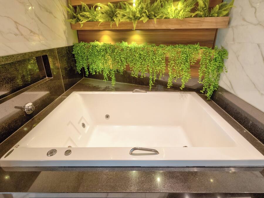 A modern bathroom with a large bathtub, green hanging plants, and a wooden shelf above the bathtub.