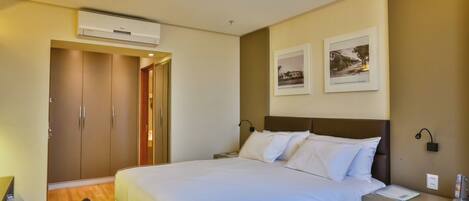 Habitación de hotel con cama, escritorio, silla, armario y dos cuadros en la pared.