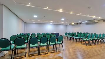 A conference room with rows of green chairs, wooden flooring, and recessed ceiling lights.