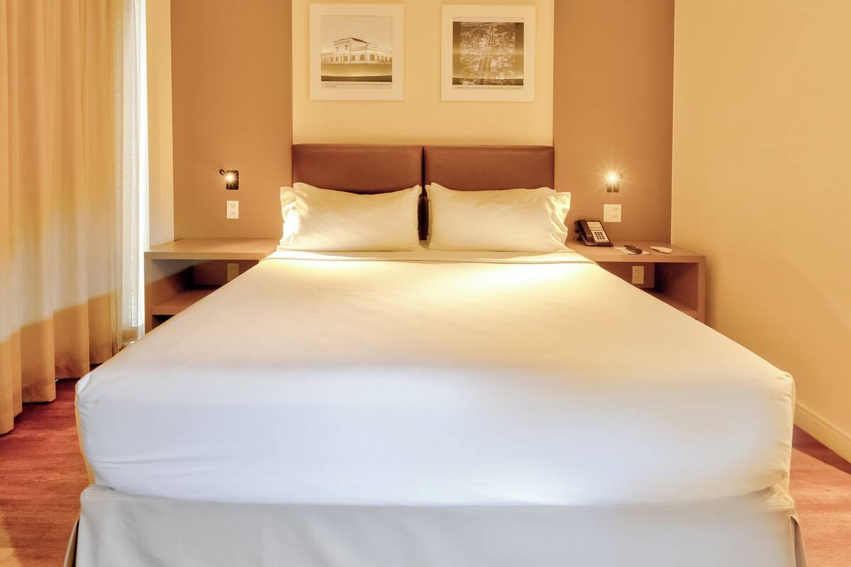 A neatly made bed with white linens, two bedside tables with lamps, and two framed pictures on the wall.