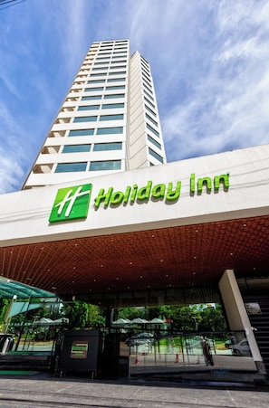 The exterior of a Holiday Inn hotel with a prominent green logo, a modern facade, and a covered entrance area.