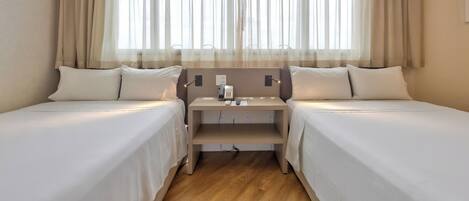 A hotel room with two single beds, a bedside table with a phone, and a window with sheer curtains.