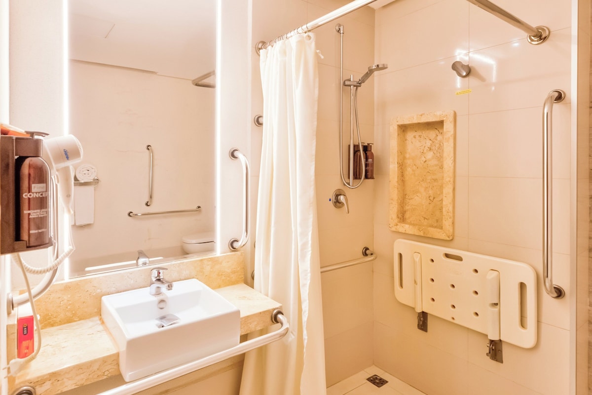 A bathroom with a sink, mirror, shower, and grab bars.