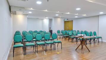 A conference room with rows of green chairs, a wooden table with a projector, and a wooden door in the background.