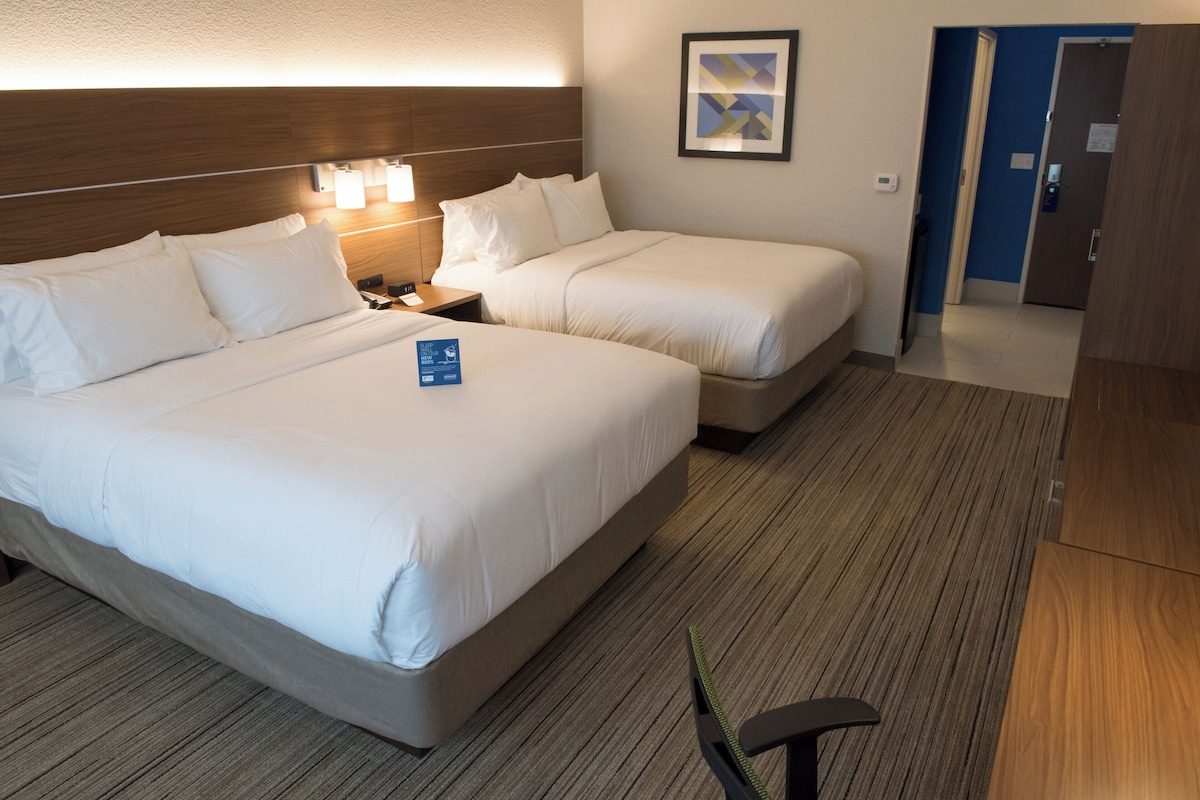 A hotel room with two beds, a nightstand, a framed picture on the wall, and a door to the right.