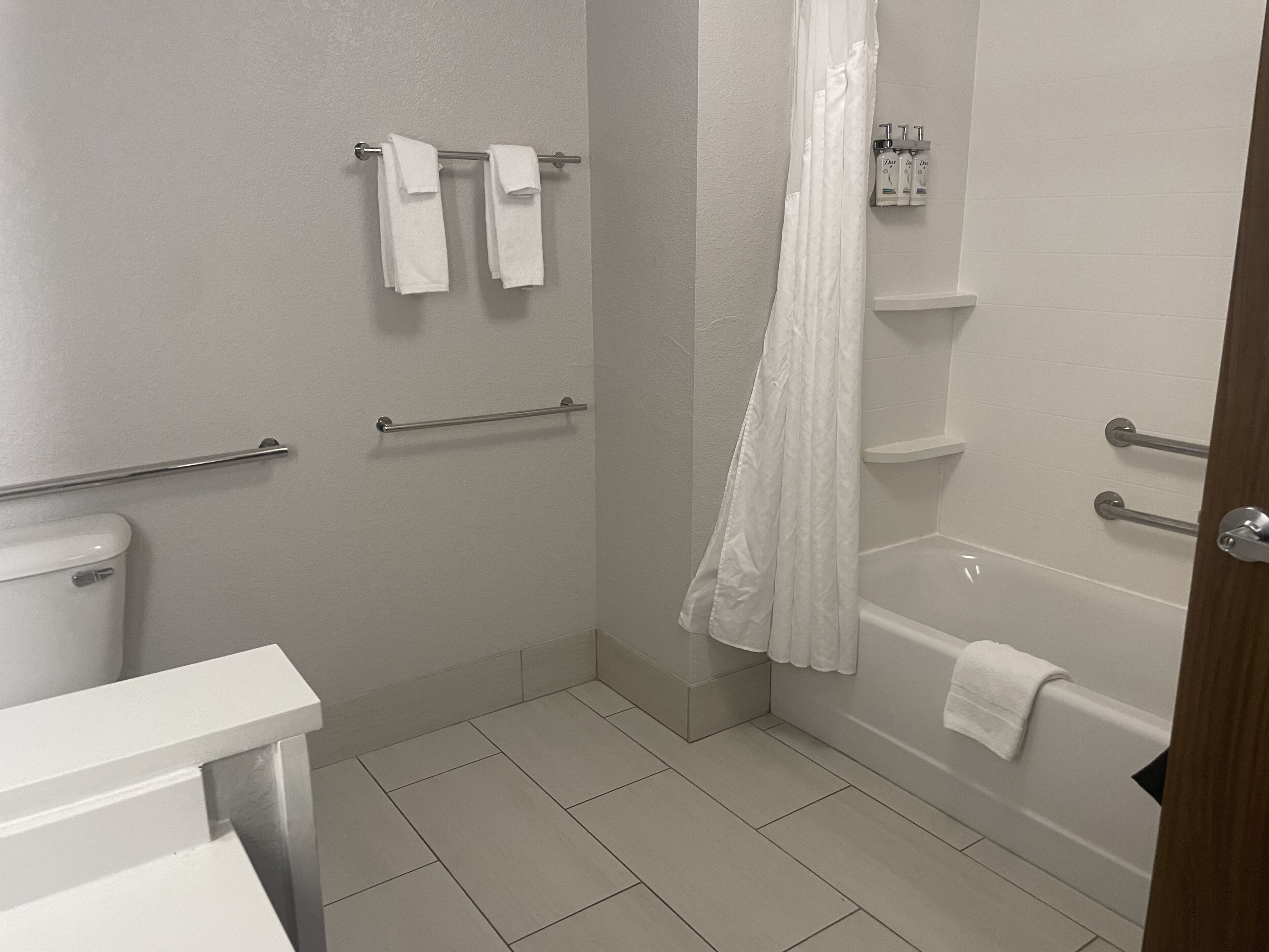 Un baño con inodoro, ducha con cortina blanca, bañera y barra de apoyo.