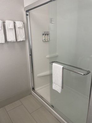 A modern bathroom with a glass shower enclosure, a white towel rack, and a glass shelf with toiletries.