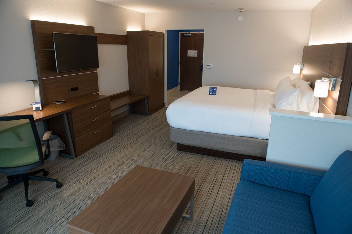 A hotel room with a bed, a desk with a chair, a TV, and a sofa.