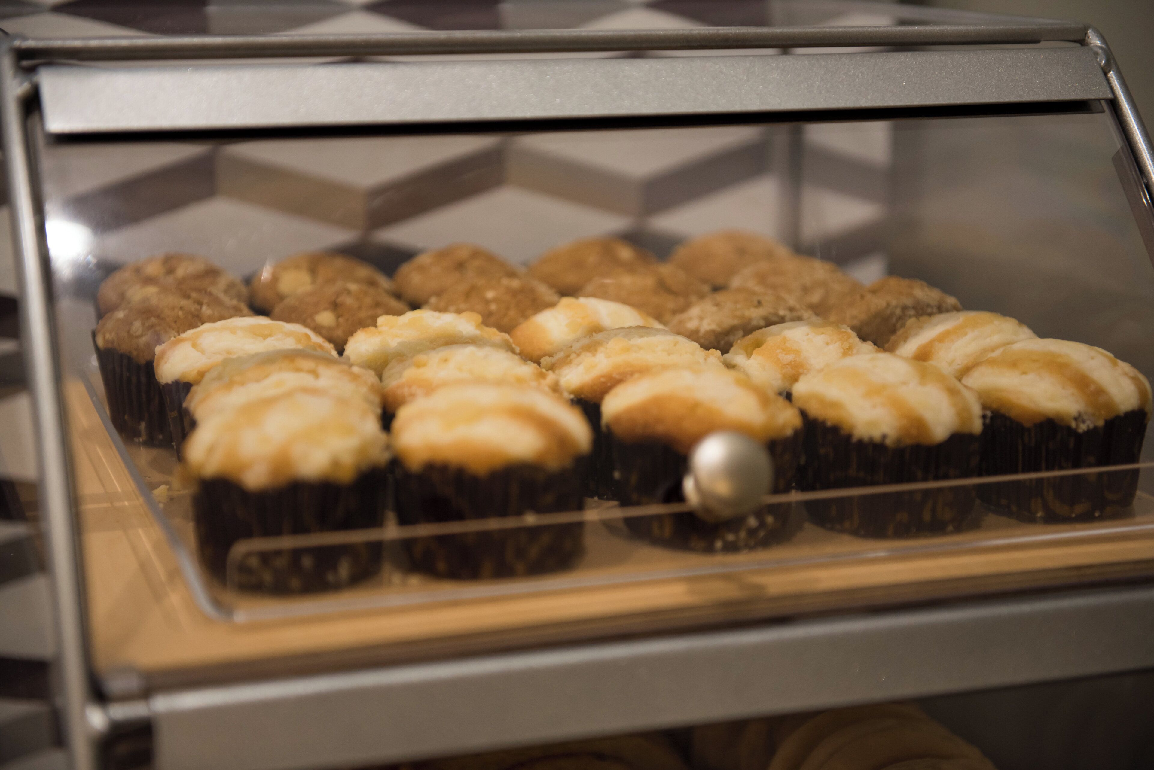 Una vitrina exhibe varias opciones de panadería, probablemente magdalenas o pasteles, con una rejilla metálica y una superficie reflectante arriba.