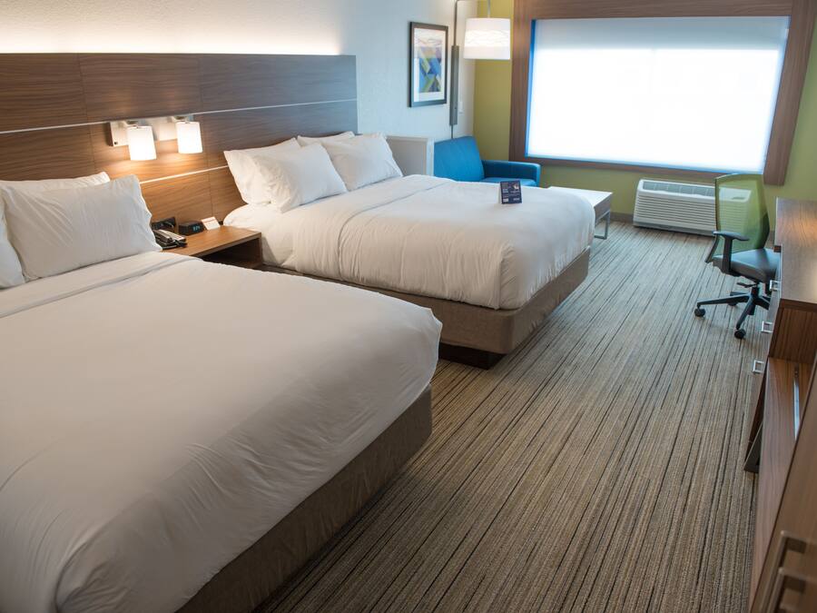 A hotel room with two beds, a desk, a chair, and a large window.