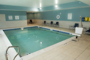 Una piscina con una silla de salvavidas, sillas de descanso y un cartel con las normas de la piscina.