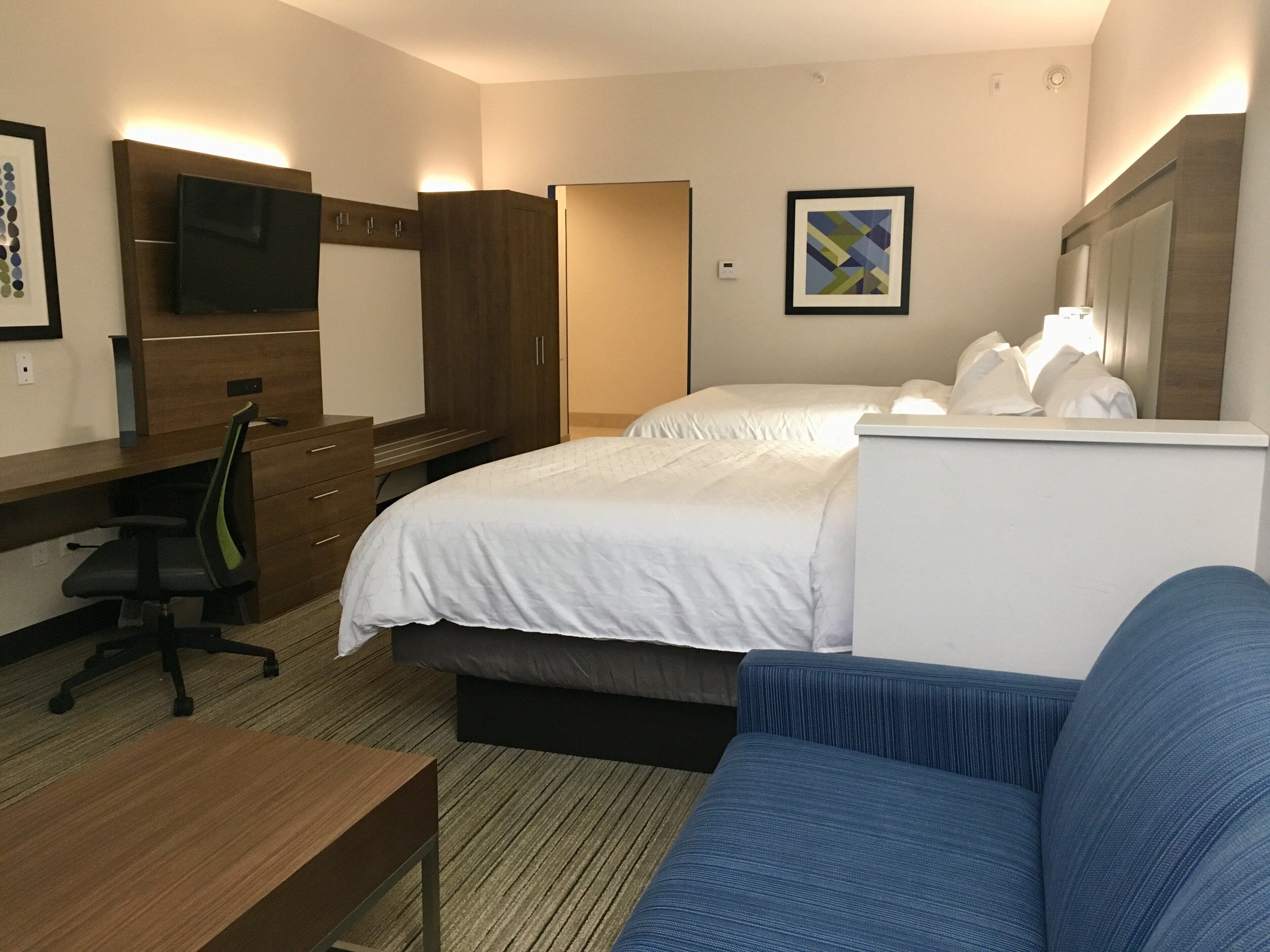 A hotel room with a bed, a desk, a chair, a TV, and a bathroom door.