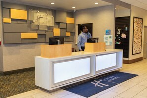 A reception desk with a modern design, a security camera above, and a blue mat with the hotel name. - Holiday Inn Express Grand Island - Niagara Falls by IHG (Grand Island)