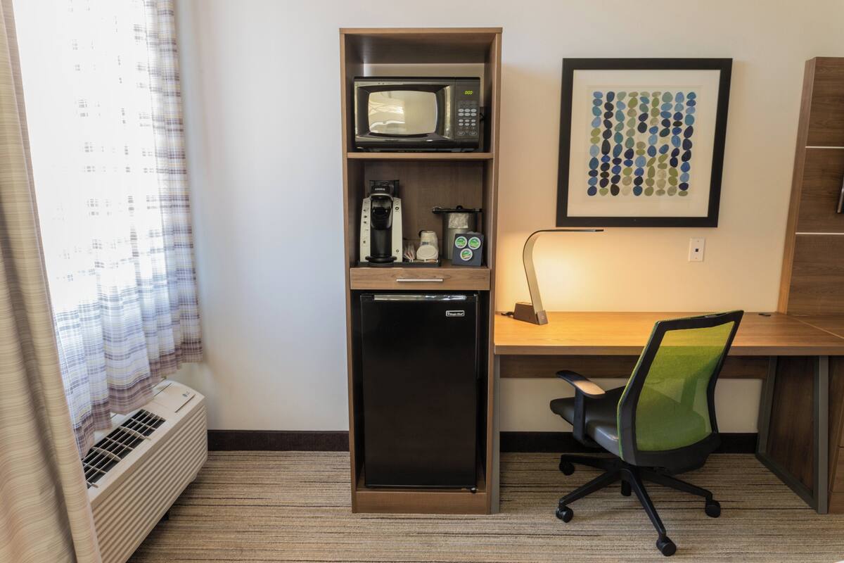 Une chambre d’hôtel compacte comprenant un coin cuisine, un bureau, une chaise et une œuvre d’art encadrée au mur.