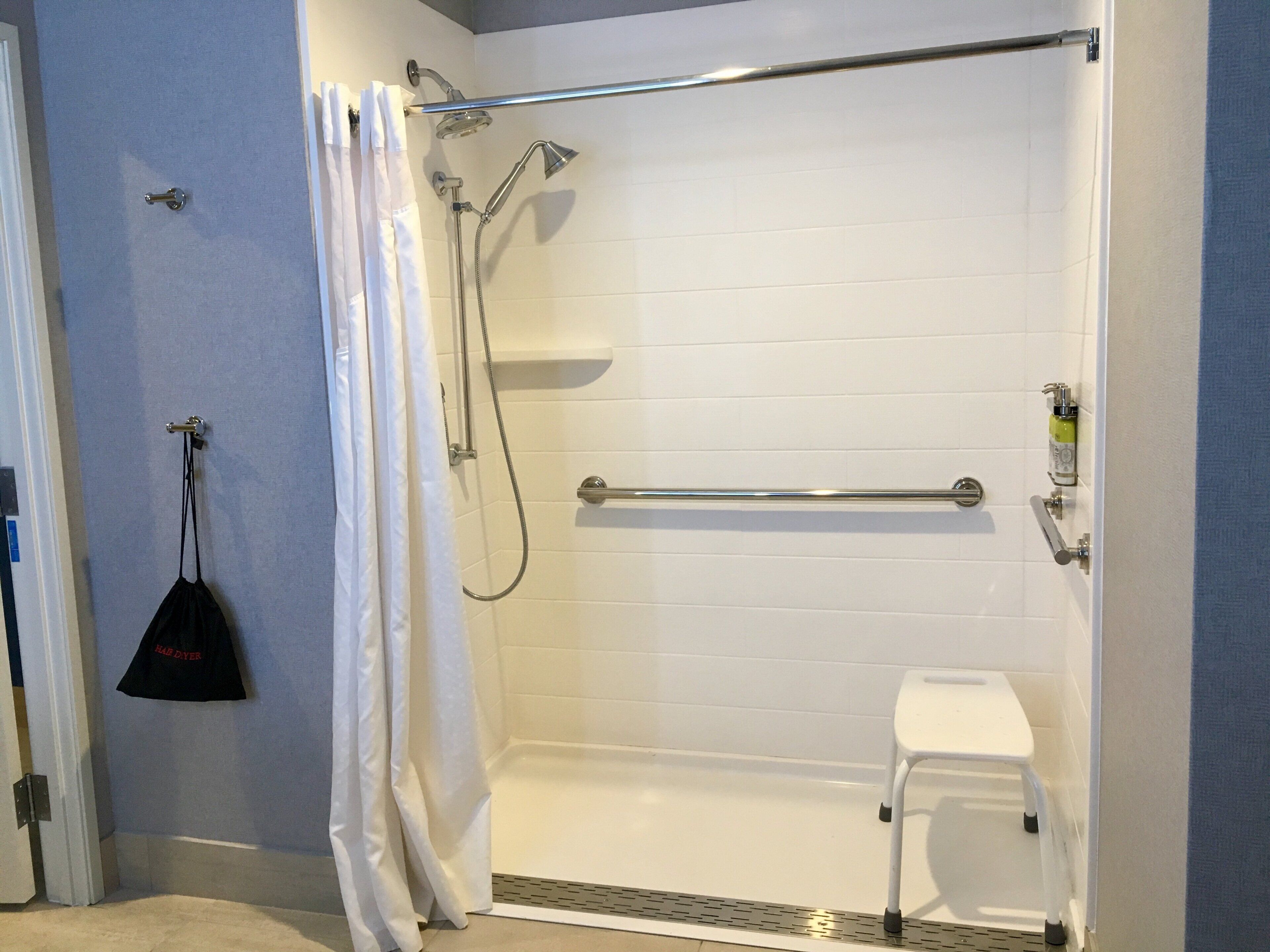 A shower area with a white bathtub, a showerhead, a handheld shower attachment, and a small white stool.
