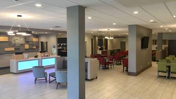 A modern hotel lobby with a reception desk, seating areas, and a bar.