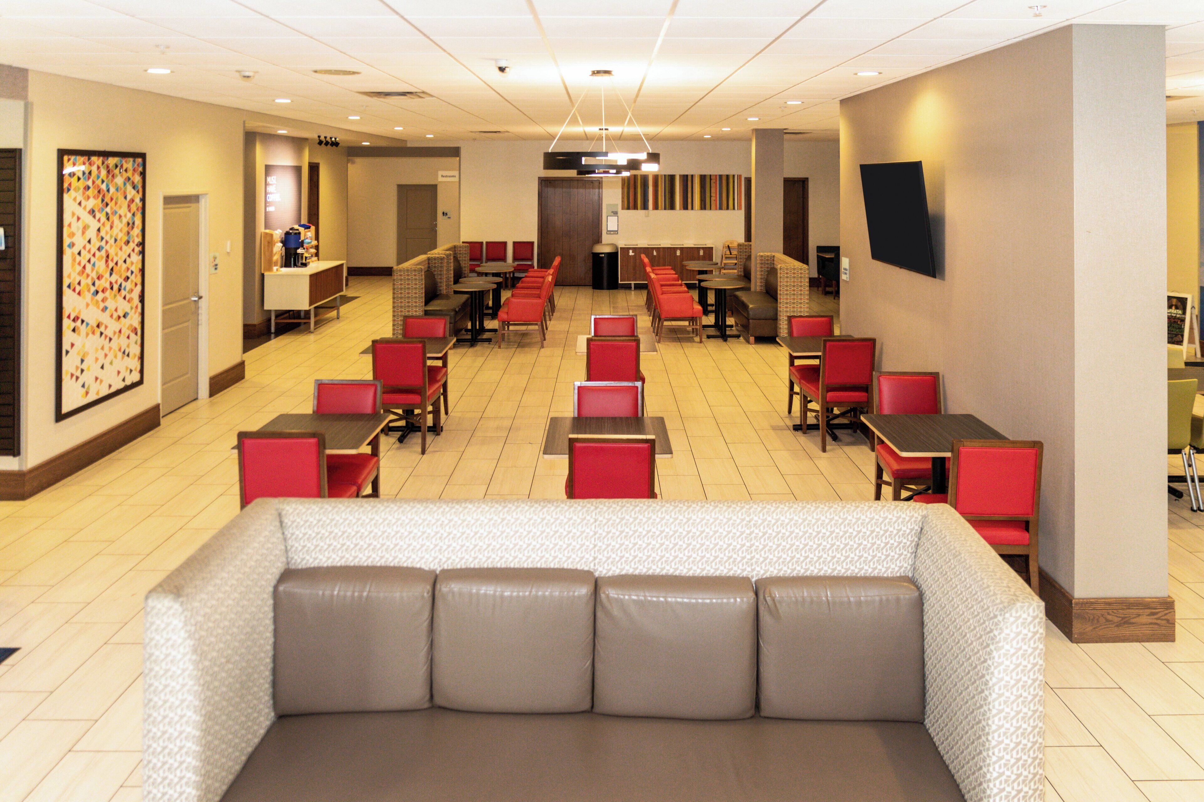 A hotel lobby with multiple seating areas, including red chairs and tables, and a large sofa.