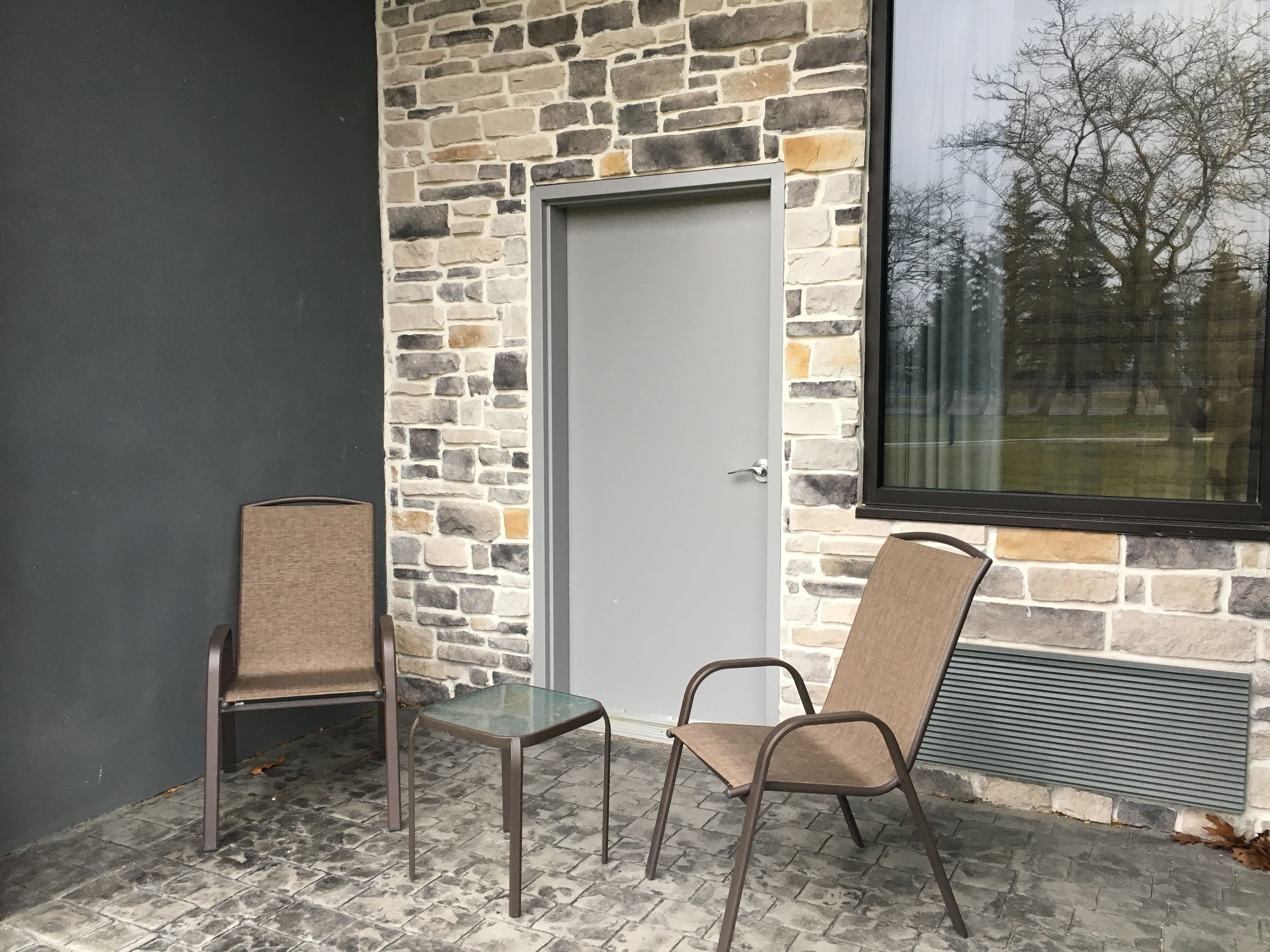 A stone wall exterior with a door, two metal chairs, and a small table.