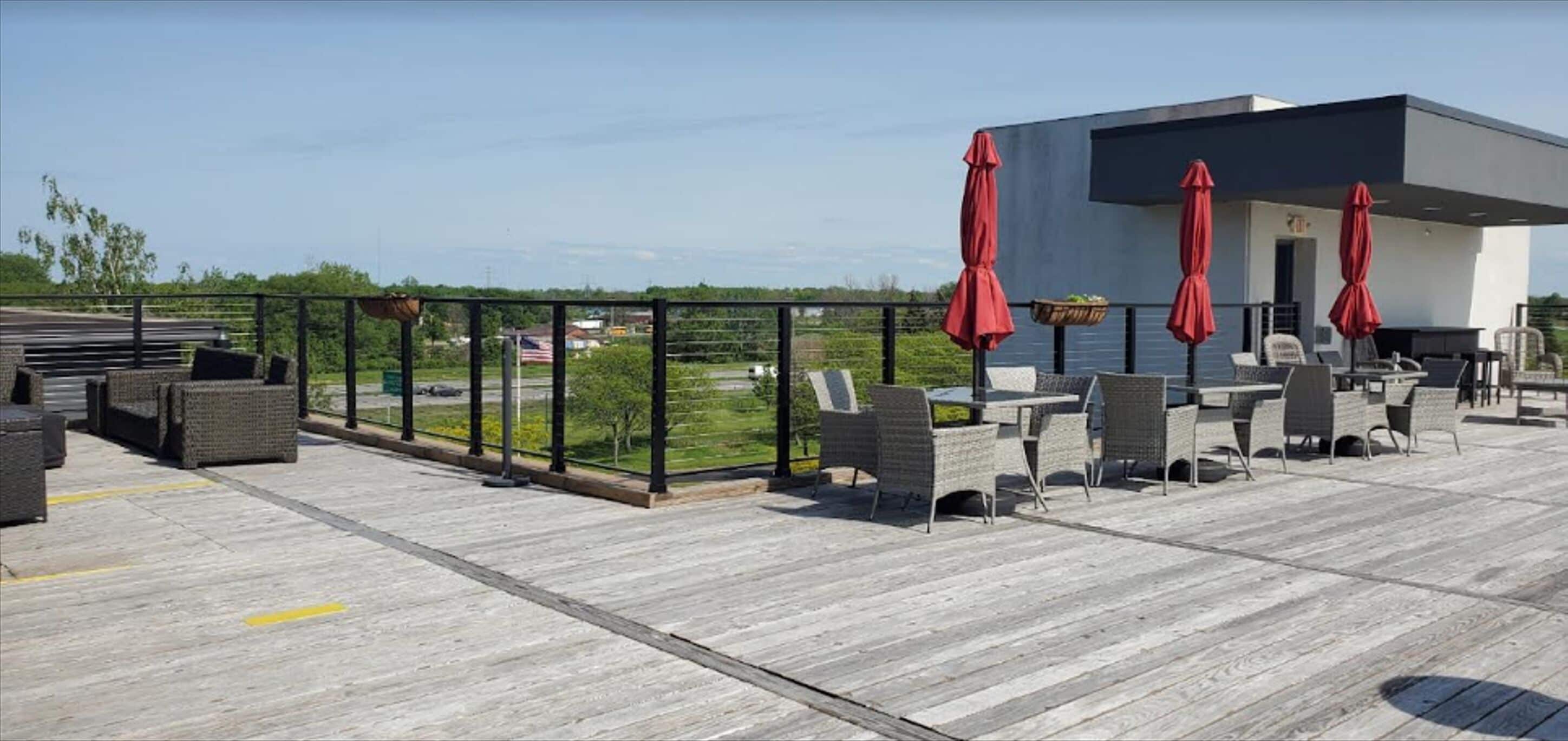 An outdoor patio with wicker furniture, red umbrellas, and a view of the cityscape.