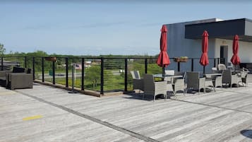 An outdoor patio with wicker furniture, red umbrellas, and a view of the cityscape.