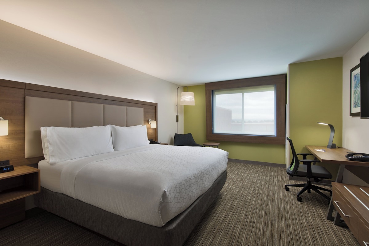 A hotel room with a bed, desk, chair, lamp, and a window.