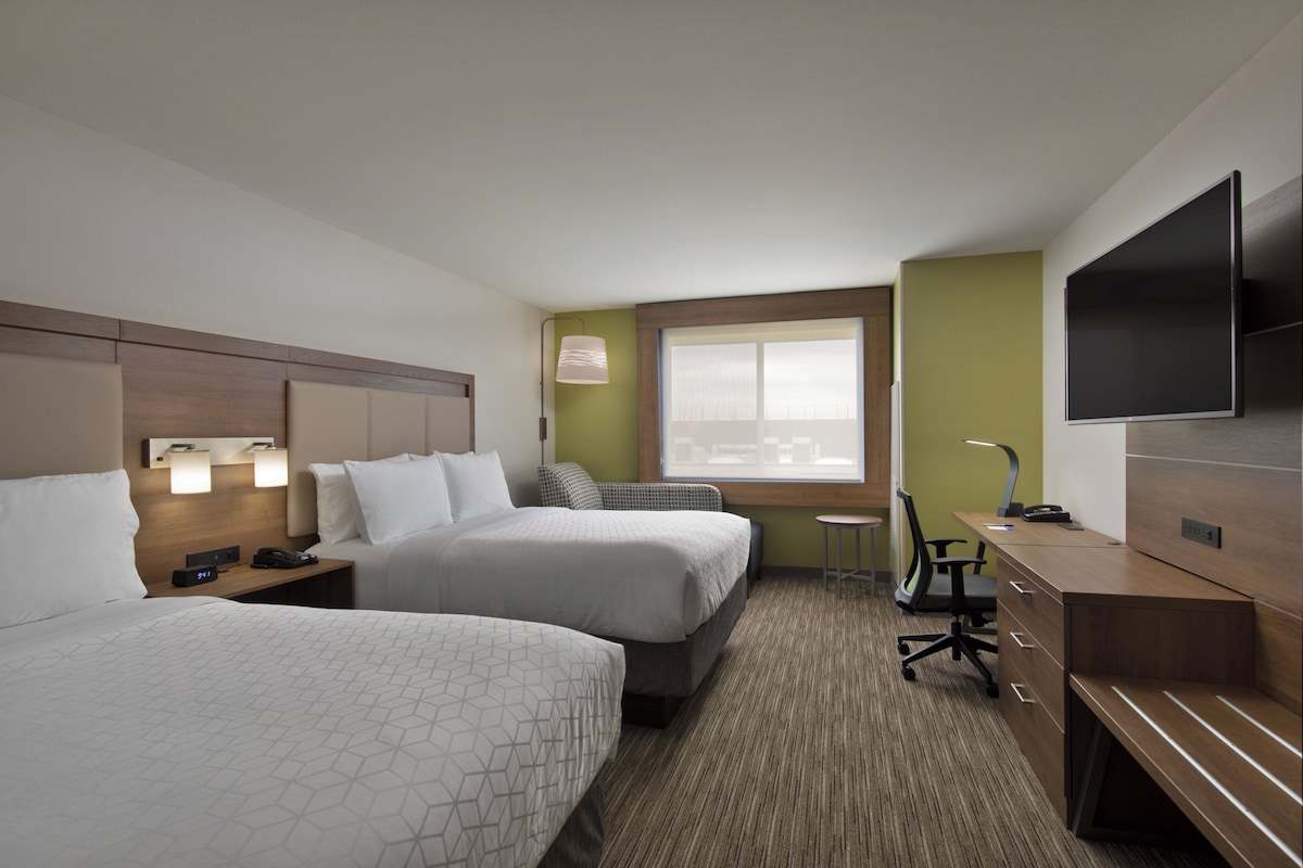 A hotel room with two beds, a desk, a chair, a TV, and a window.