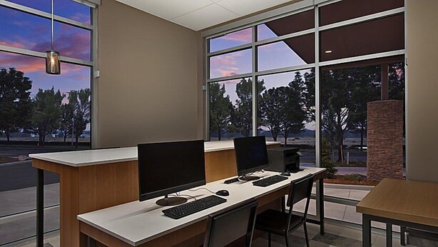 A modern office space with two desks, computers, and a view of trees and sky through large windows. - Holiday Inn Express & Suites Portland Airport - Cascade Stn by IHG (Portland)