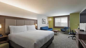 A hotel room with a large bed, a desk, a chair, a sofa, and a window.