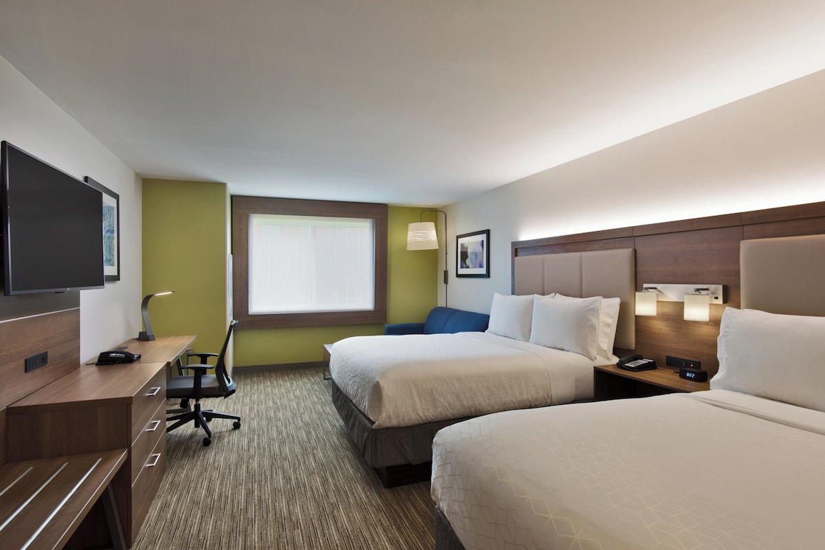 A hotel room with two beds, a desk with a chair, a TV, and a window.