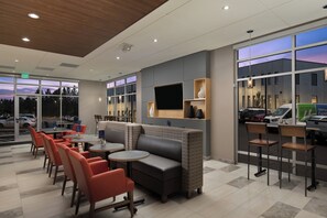 A modern indoor seating area with tables and chairs, a sofa, and a TV screen mounted on the wall. - Holiday Inn Express & Suites Portland Airport - Cascade Stn by IHG (Portland)